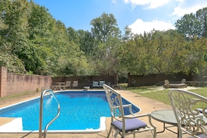 A backyard with a swimming pool, surrounded by trees and a brick wall.