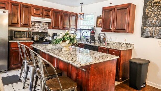 A kitchen with wooden cabinets, a granite countertop, a stainless steel refrigerator, a microwave, and a sink.