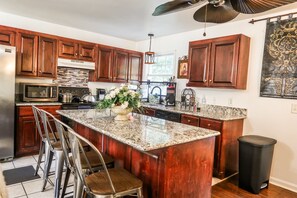 A kitchen with wooden cabinets, a granite countertop, a stainless steel refrigerator, a microwave, and a sink.