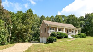 A two-story house with a front porch, surrounded by a grassy yard and dense trees.
