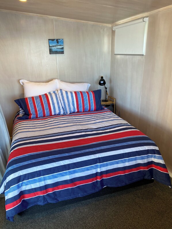 Een bed met een gestreepte spreidekker, een nachtkastje met een lamp, en een klein schilderij aan de muur.
