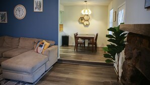 Un salon avec un canapé, un coin repas avec une table et des chaises, et un escalier menant à une autre pièce.