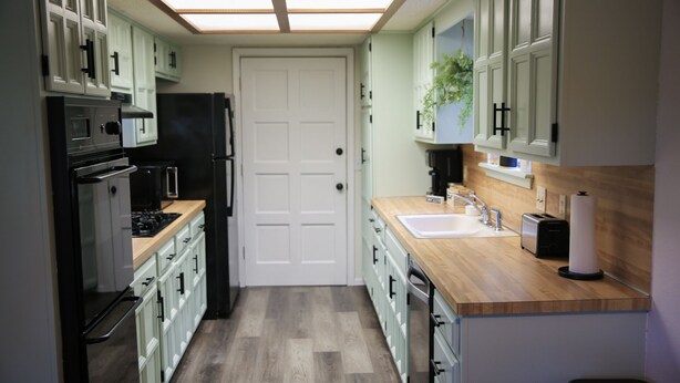 Une cuisine compacte avec des meubles blancs, un réfrigérateur noir, un plan de travail en bois et un four encastré.