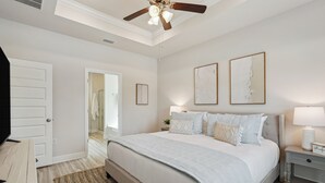 Una camera da letto con un letto grande, una ventola a soffitto, un comodino con una lampada e una porta che dà su un'altra stanza.