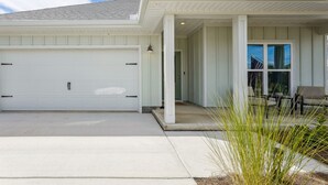 Una casa a un piano con un portone da garage bianco, un portico coperto e un ingresso che dà su un’area relax con mobili da esterno.
