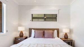 A bedroom with a large bed, two bedside tables, a window with blinds, and a ceiling light.