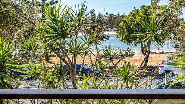 A coastal view with a beach, parked cars, and tropical vegetation.