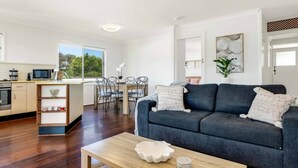 A modern living room with a dark grey sofa, wooden coffee table, and a dining area with a wooden table and chairs.