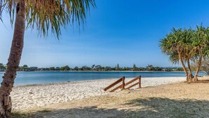 A beach with a wooden fence, palm trees, and a clear blue sky.