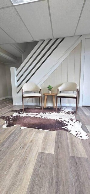 A room with a wooden floor, a cowhide rug, two chairs, a small table with a plant, and a staircase in the background. - 25-Acre Farm Stay w/ Hot Tub & Fire Pit (Harrison)