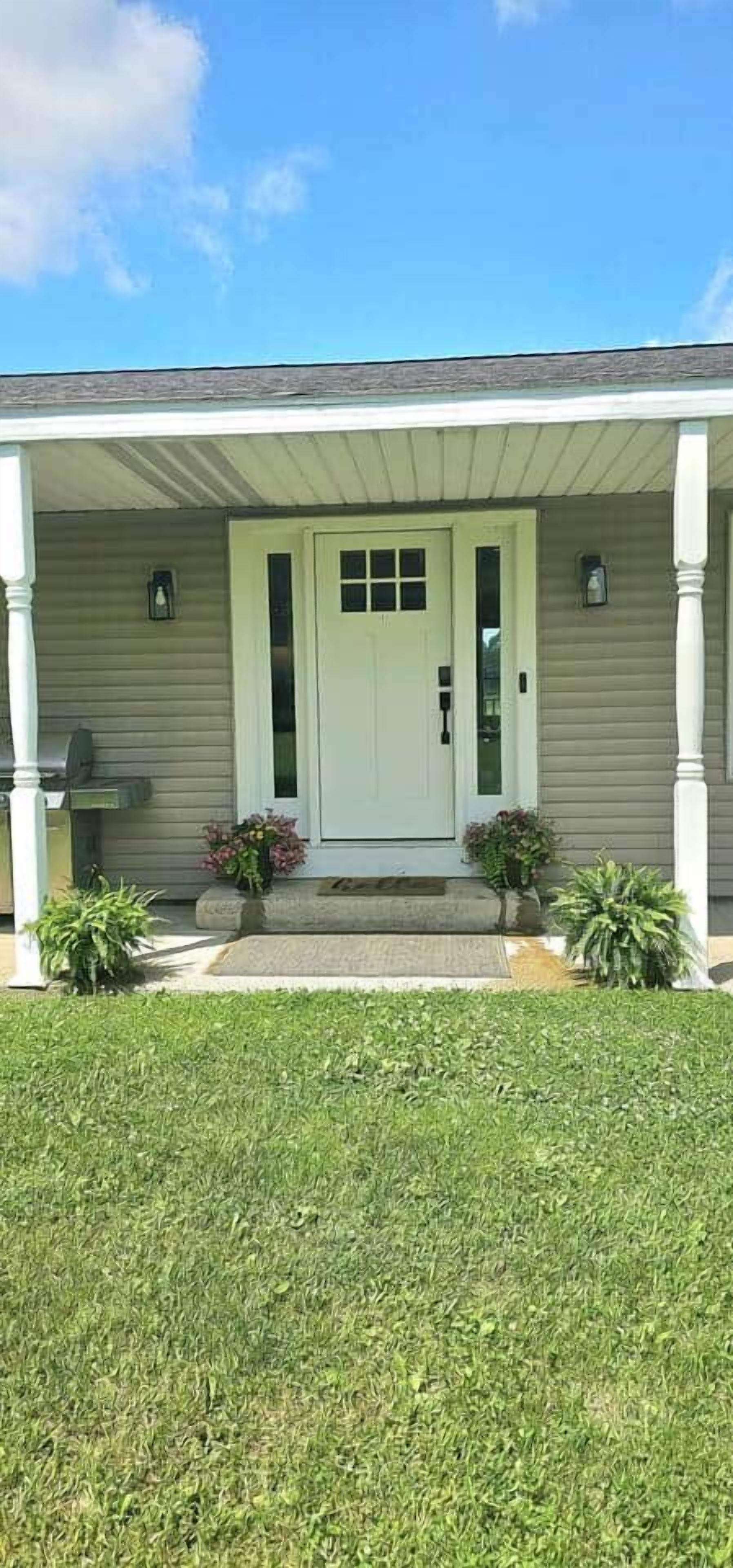 A house with a front porch, a white door, and a small front yard with grass and potted plants.