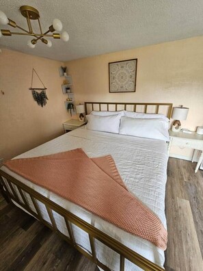 Un dormitorio con cama, mesitas de noche, una lámpara colgante y una obra de arte enmarcada en la pared.