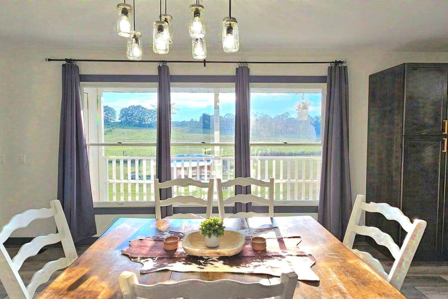 Ein Essbereich mit Holztisch, weißen Stühlen, einer Pendelleuchte und Blick auf einen umzäunten Garten durch große Fenster.