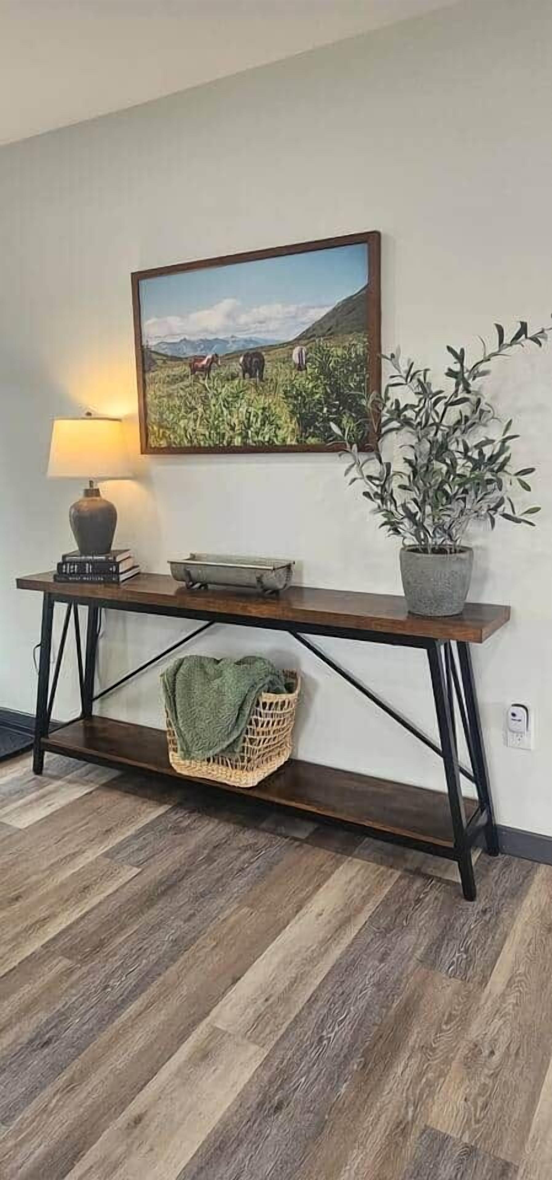 A wooden console table with a woven basket, a potted plant, and a framed landscape painting above it.
