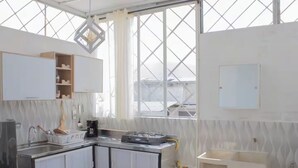 Une cuisine moderne avec des meubles blancs, une cuisinière à gaz et une fenêtre donnant sur des immeubles.