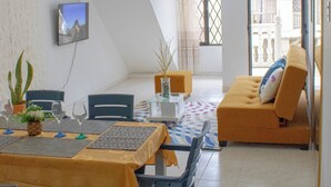 Un coin repas avec une table dressée pour quatre personnes, un canapé et un téléviseur fixé au mur.