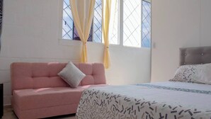 Une chambre avec un canapé rose, un lit avec une literie à motifs et une fenêtre avec des rideaux.
