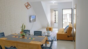 Un coin repas avec une table dressée pour quatre personnes, des chaises, un canapé et un téléviseur fixé au mur.