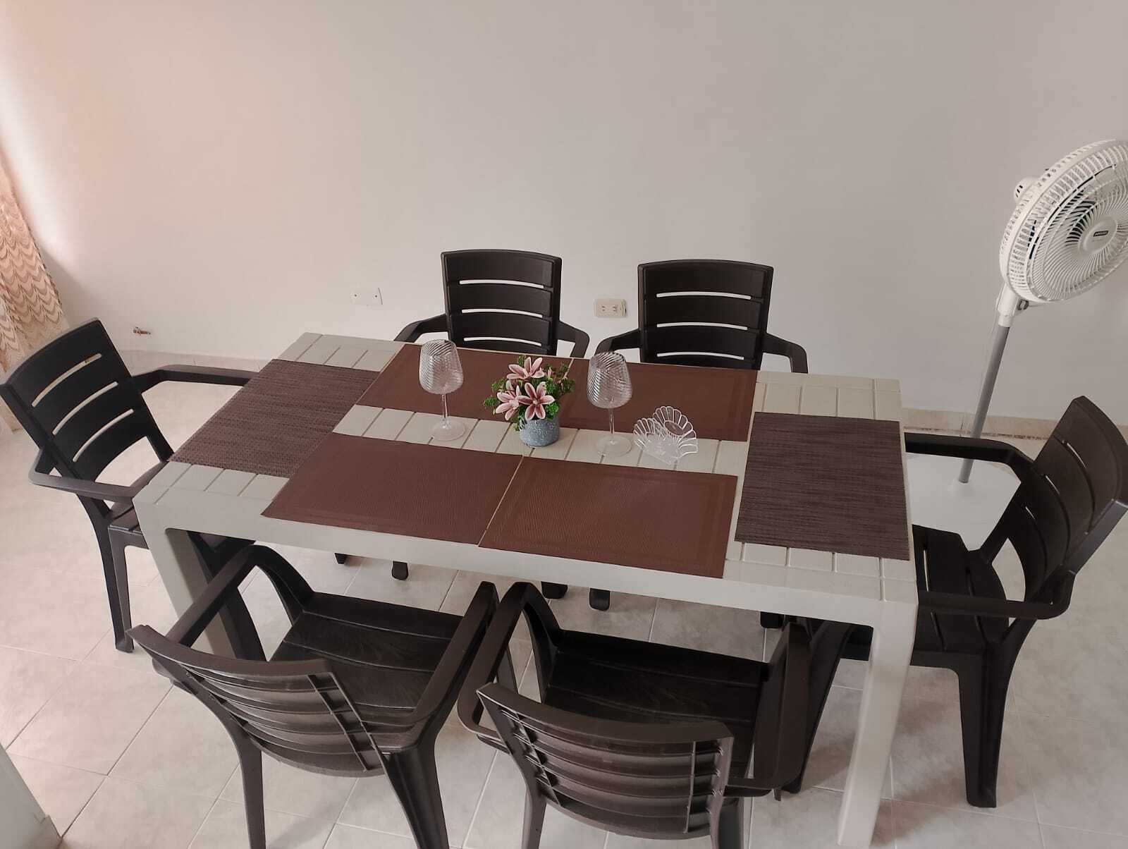 Une table à manger avec un set de table marron, des chaises noires et un ventilateur blanc.