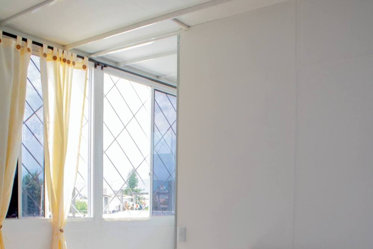Une chambre à coucher avec un lit, une chaise, une fenêtre avec des rideaux et une vue sur l’extérieur.