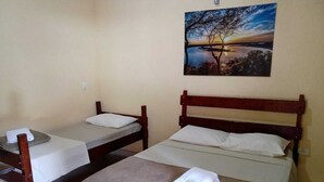 A simple room with two wooden beds, a small table, and a painting of a sunset on the wall. - Pousada Sol e Lua (Caraguatatuba)