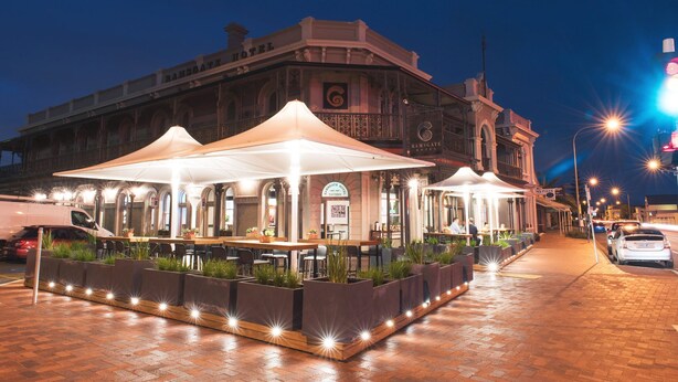 A historic building with a restaurant patio featuring outdoor seating and a large umbrella. - Enjoy beachside vibes at beautiful Henley Beach! (Henley Beach)