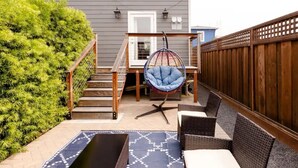 A patio with a hanging chair, wicker furniture, and a staircase leading to a door. - Savor the Peace at a Comfy Cottage Minutes from Downtown SF (Myrtle Beach)