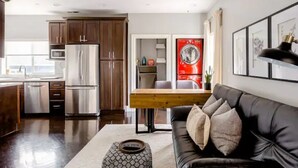 A modern kitchen with stainless steel appliances, a dining area with a wooden table, and a black leather sofa. - Savor the Peace at a Comfy Cottage Minutes from Downtown SF (Myrtle Beach)