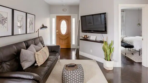 A modern living room with a leather sofa, a coffee table, and a flat-screen TV mounted on the wall. - Savor the Peace at a Comfy Cottage Minutes from Downtown SF (Myrtle Beach)