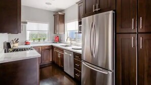 A modern kitchen with dark wooden cabinets, stainless steel appliances, and a white countertop. - Savor the Peace at a Comfy Cottage Minutes from Downtown SF (Myrtle Beach)