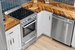 A kitchen with a built-in stove, oven, and dishwasher, featuring a herringbone wood countertop and white cabinetry. - Luxury Lake Barkley Bungalow
 (Cadiz)