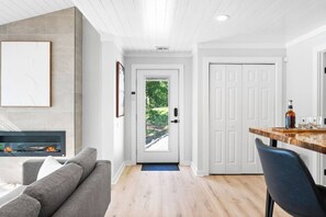 A modern living room with a fireplace, a dining area with a wooden table, and a view through a door.