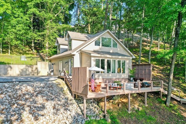 A two-story house with a deck, surrounded by trees.