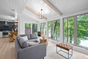 A spacious living room with a gray sectional sofa, a wooden coffee table, and a bench. Large windows offer a view of the outdoors.