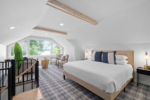 A bedroom with a large bed, a chair, a small table, and a window with a view.