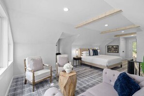 A modern bedroom with a large bed, two chairs, a small table, and a view of the outdoors. - Luxury Lake Barkley Bungalow
 (Cadiz)