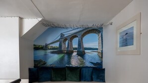 Una habitación con un gran mural de un puente sobre el agua, un cuadro enmarcado en la pared y una ventana con vistas al exterior.
