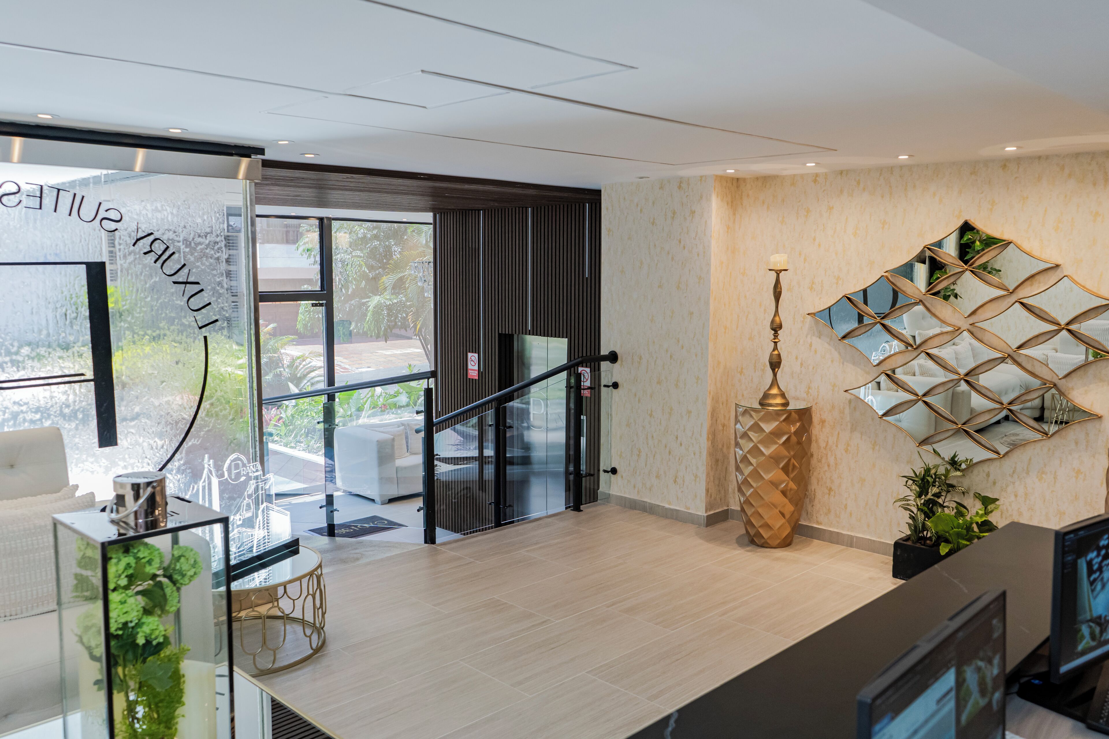 A modern hotel lobby with a glass partition, a staircase, and a decorative mirror.