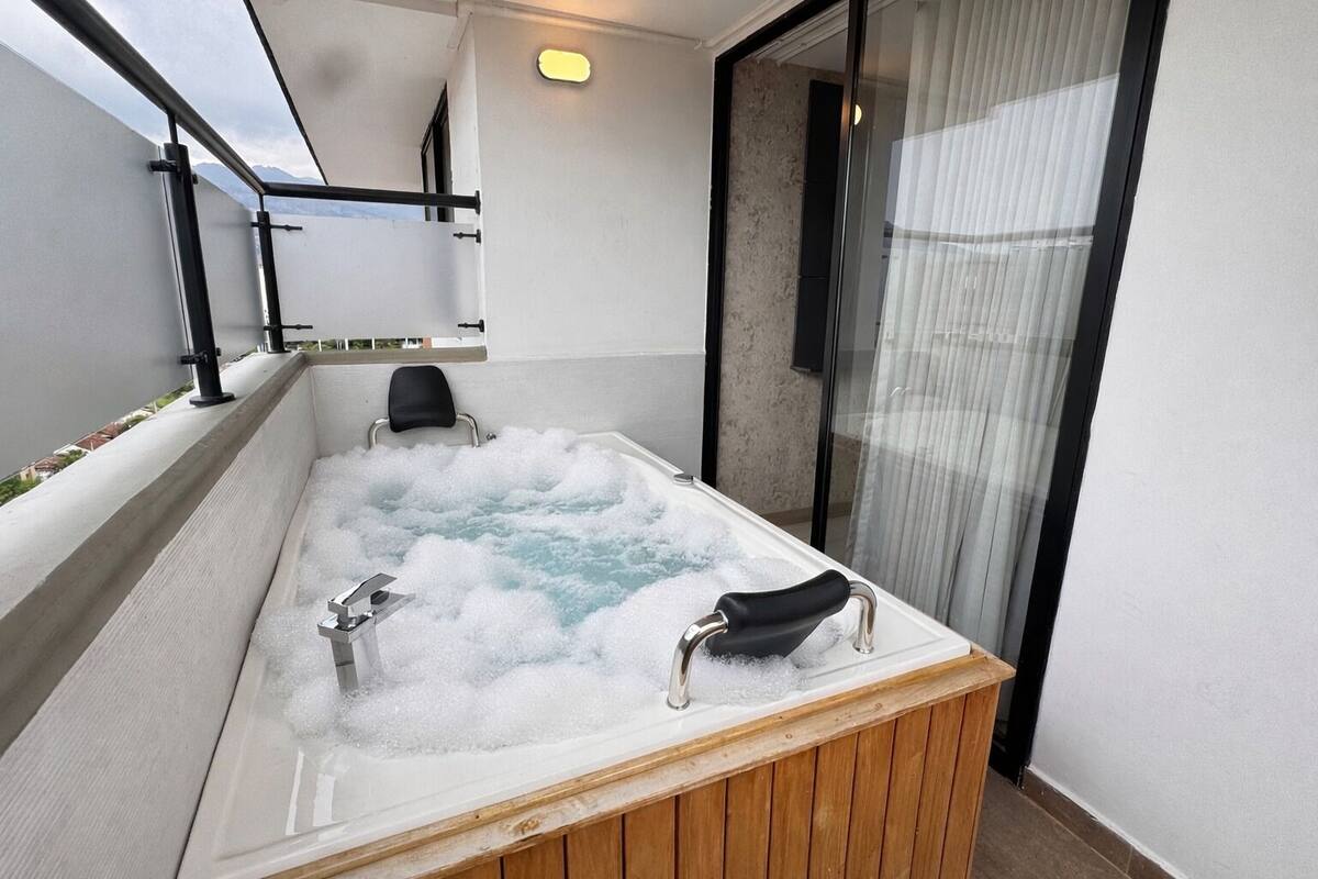 Un jacuzzi con dos sillas, una terraza de madera y un ventanal que da a un balcón.