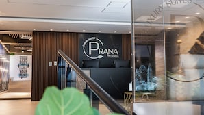 Un intérieur d’hôtel moderne avec un comptoir d’accueil, une enseigne indiquant « PRANA by Cadissa » et un mur de verre qui reflète un élément décoratif aquatique.