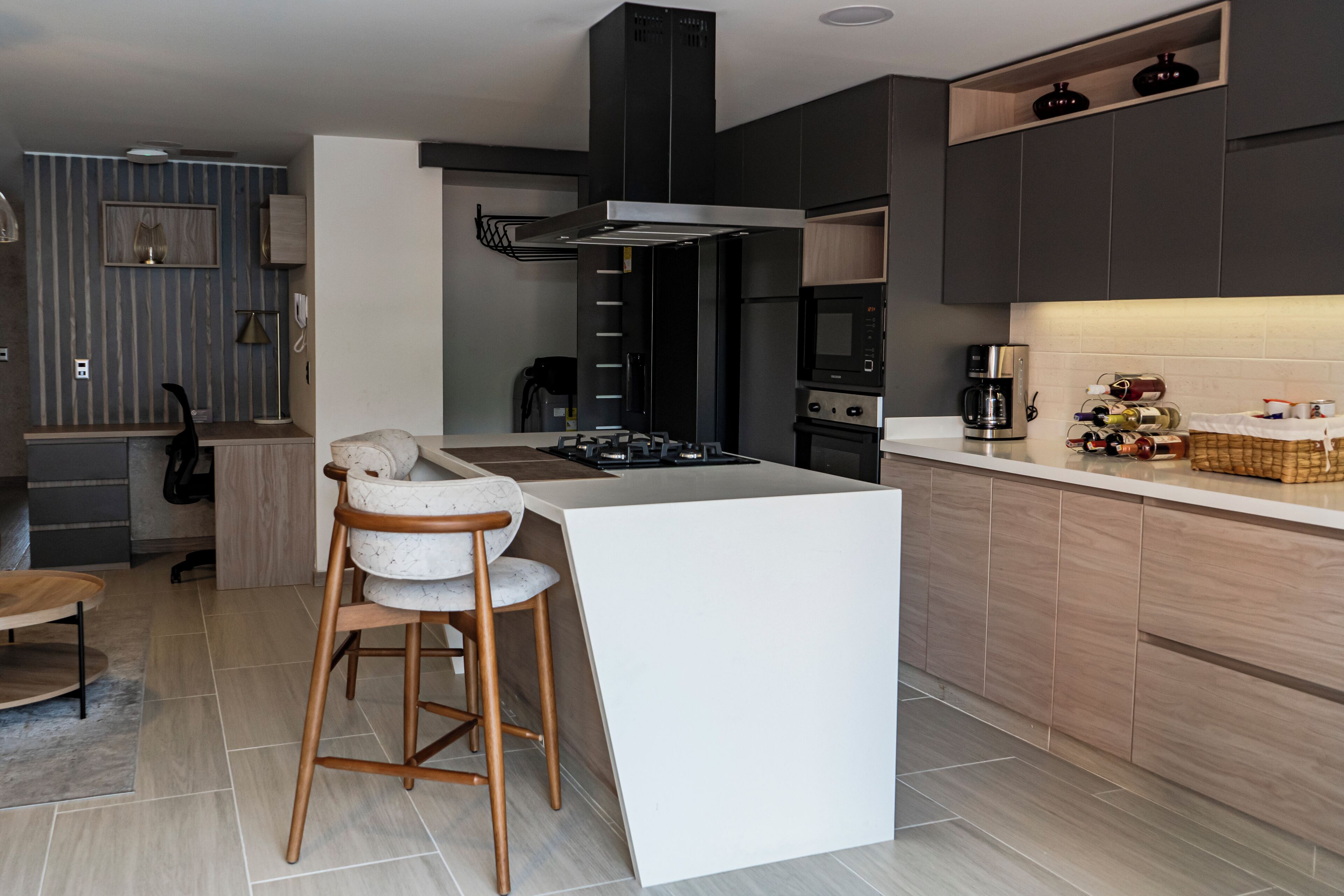 A modern kitchen with a central island, bar stools, a built-in oven, and a microwave.