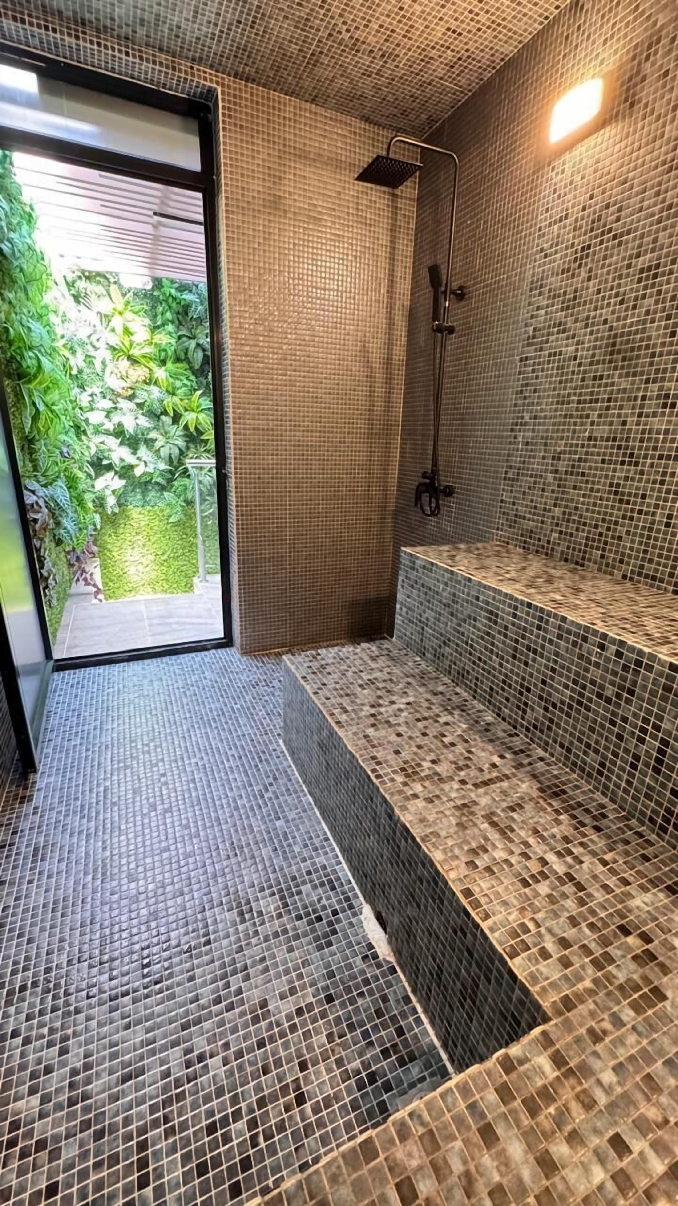 A modern bathroom with mosaic tile walls and floor, a shower area, and a bench.