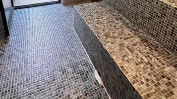 A modern bathroom with mosaic tile walls and floor, a shower area, and a bench.