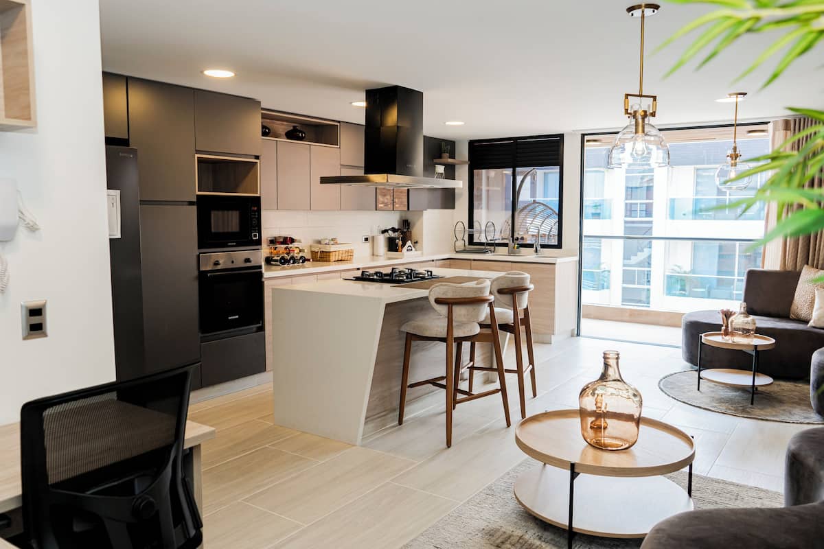 Una cocina moderna con una isla central, taburetes de bar y un comedor con una mesa redonda.