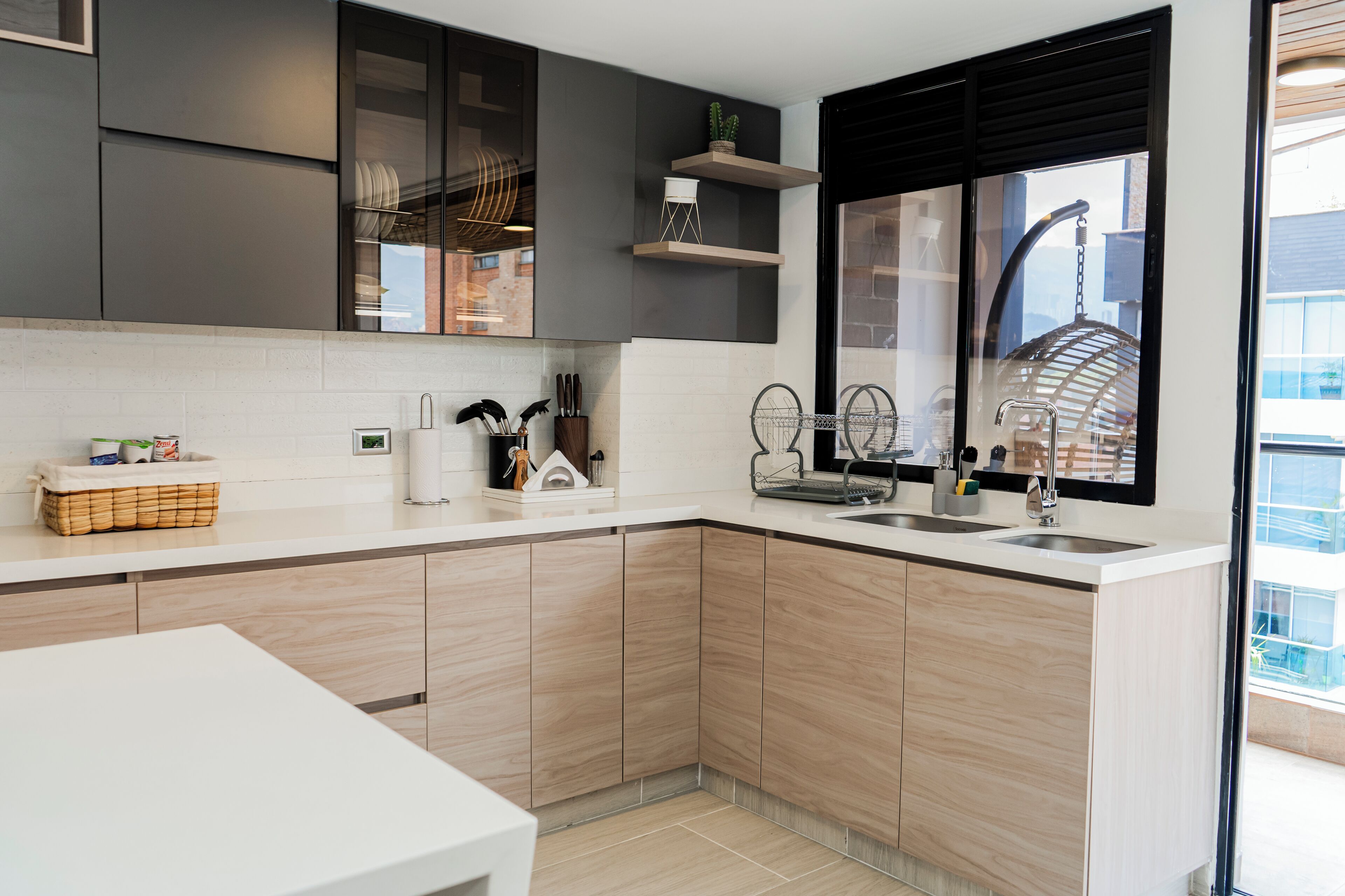 A modern kitchen with light wood cabinets, a white countertop, and a window with a view of the city.