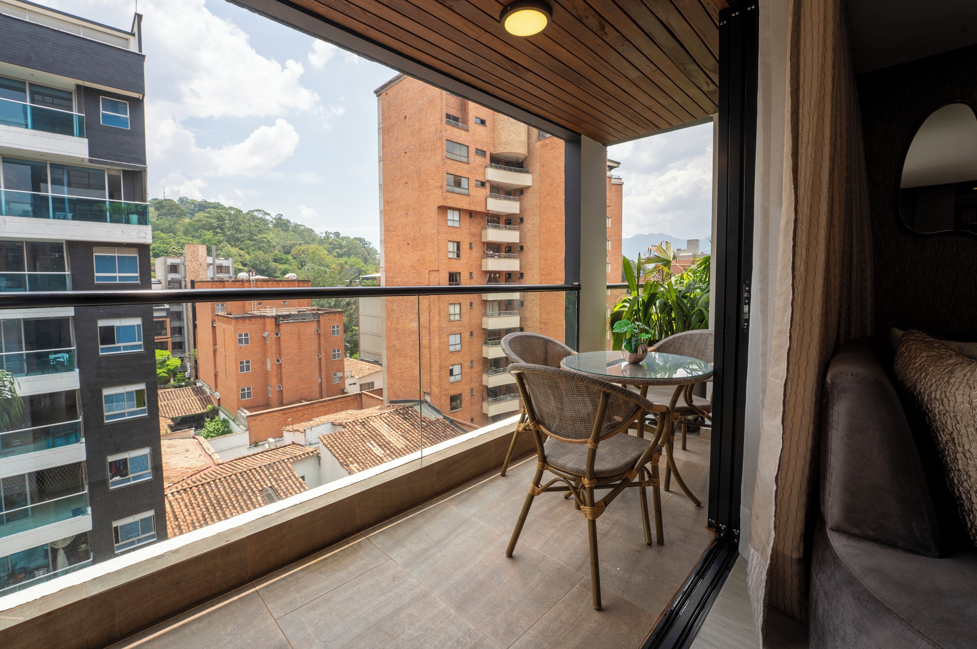 Un balcon avec une table et des chaises, un canapé et une vue sur les bâtiments environnants et la verdure.