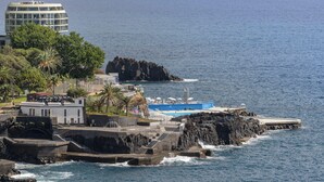 A coastal hotel with a pool area, rocky cliffs, and a view of the sea.