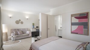 A modern bedroom with a bed, a sofa, a desk with a computer, and a TV. There is a round rug, a lamp, and wall art.