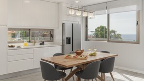 Eine moderne Küche mit weißen Schränken, einem Holzespeisetisch und Blick aufs Meer.
