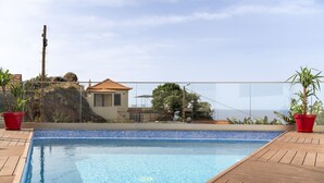 Ein Pool mit einer gefliesten Kante, einem Holzboden und roten Pflanzgefäßen.